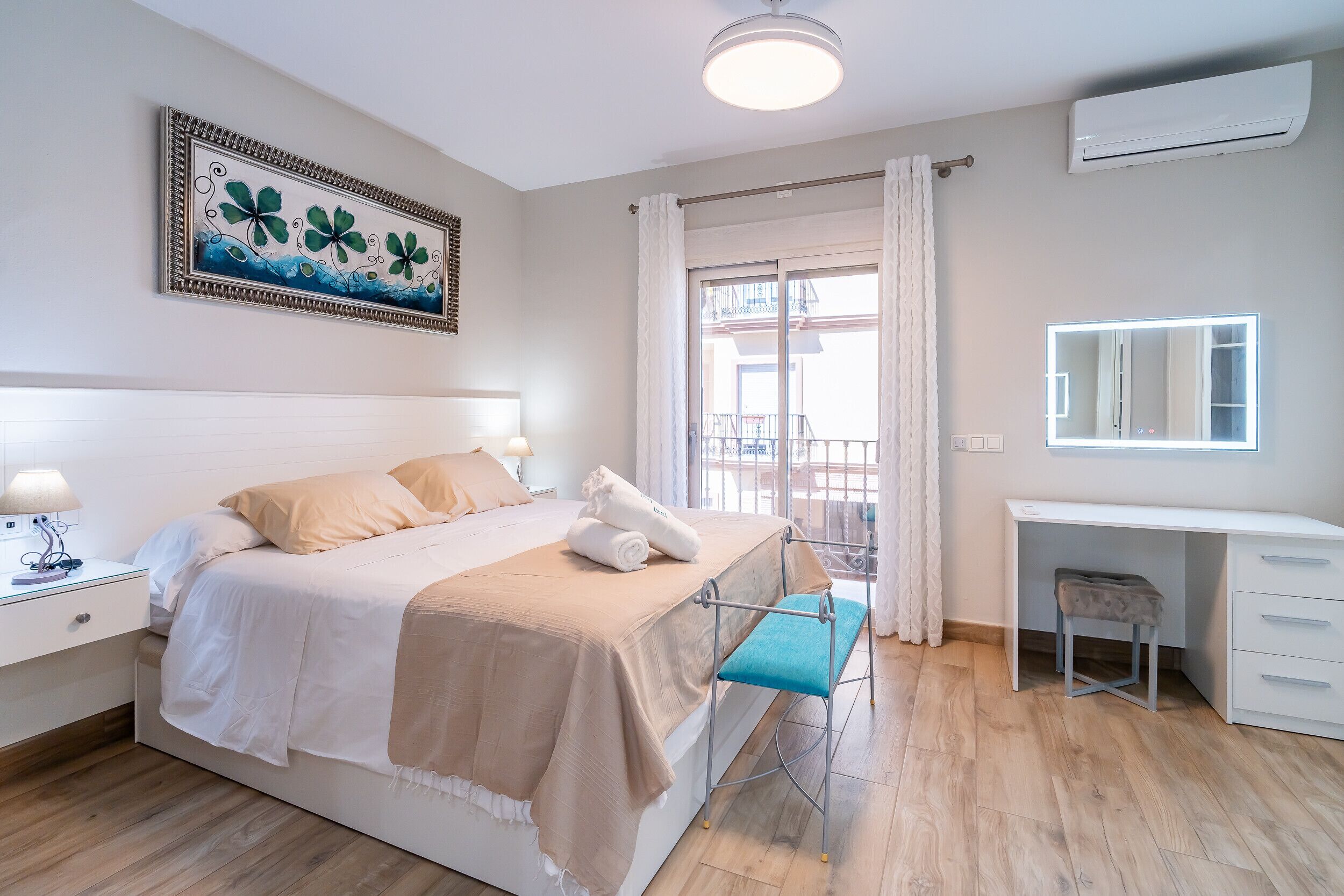 Ein Hotelzimmer mit Bett, Nachttisch, Lampe, Schreibtisch mit Stuhl, Fenster mit Vorhängen und einer Wand-Klimaanlage.