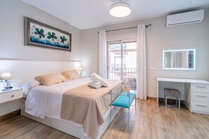 A hotel room with a bed, bedside table, lamp, a desk with a chair, a window with curtains, and a wall-mounted air conditioning unit. - Cubo's Urban Plaza Apartment / urban / air conditioning / terrace / free wifi (Alhaurín el Grande)