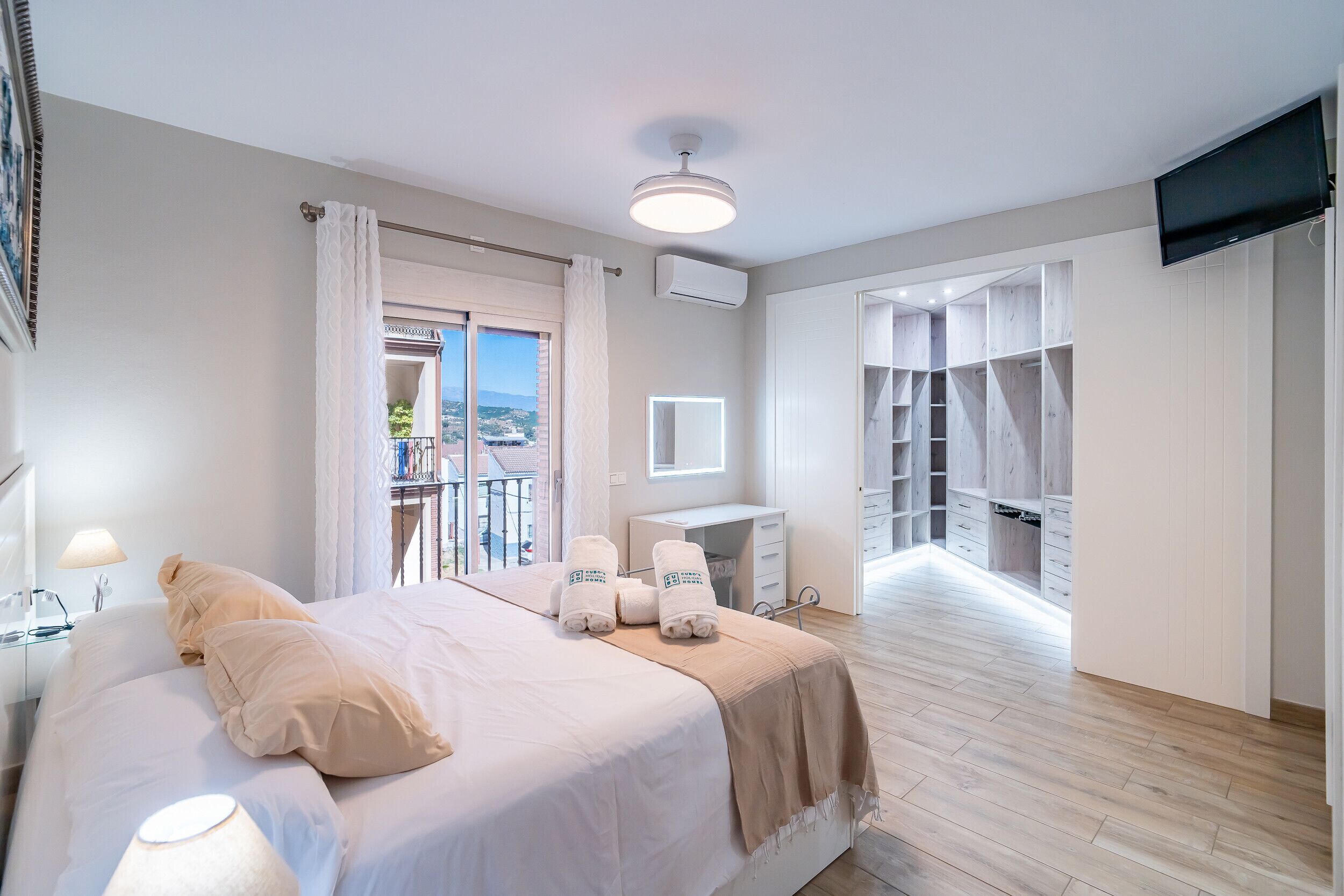 A hotel room with a bed, a desk, a TV, and a balcony with a view.