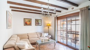 Un soggiorno con un divano angolare beige, un tavolino in vetro, un lampadario e un'ampia finestra con vista su un balcone.