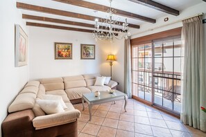 A living room with a beige sectional sofa, a glass coffee table, a chandelier, and a large window with a view of a balcony. - Cubo's Urban Plaza Apartment / urban / air conditioning / terrace / free wifi (Alhaurín el Grande)