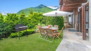 An outdoor patio with a table and chairs, a barbecue grill, and a view of mountains. - Appartamento Fior di Roccia (Bardonecchia)