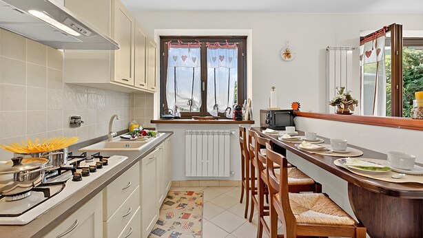 A compact kitchen with a gas stove, sink, and a window with curtains. - Appartamento Fior di Roccia (Bardonecchia)