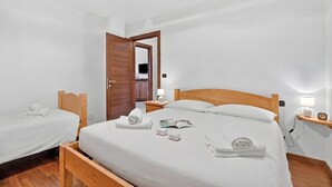A hotel room with a single bed, two bedside tables, a wooden headboard, a nightstand, a lamp, and a wall-mounted TV. - Appartamento Fior di Roccia (Bardonecchia)
