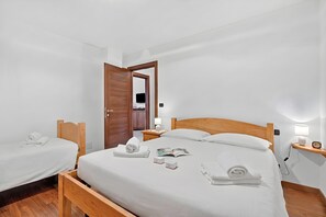 A hotel room with a single bed, two bedside tables, a wooden headboard, a nightstand, a lamp, and a wall-mounted TV. - Appartamento Fior di Roccia (Bardonecchia)