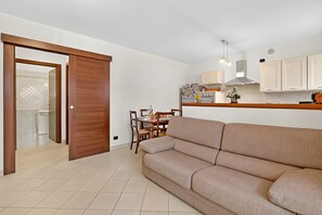 Eine moderne Küche mit weißen Schränken, ein Essbereich mit Holztisch und -stühlen sowie ein beiges Sofa in einem Wohnzimmer.