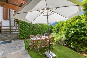 An outdoor dining area with a table set for four, surrounded by wooden chairs, under a large white umbrella. - Appartamento Fior di Roccia (Bardonecchia)