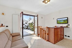 A modern living room with a sofa, a wooden dining table, and a television mounted on the wall. - Appartamento Fior di Roccia (Bardonecchia)