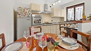 A compact kitchen with a dining area, equipped with a refrigerator, oven, and a window with curtains. - Appartamento Fior di Roccia (Bardonecchia)