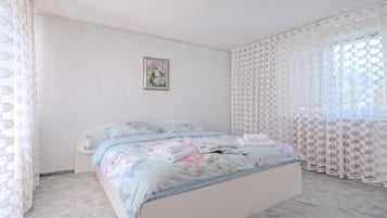 Une chambre à coucher avec un lit, une table de chevet, une fenêtre avec des rideaux à motifs et un tableau accroché au mur.