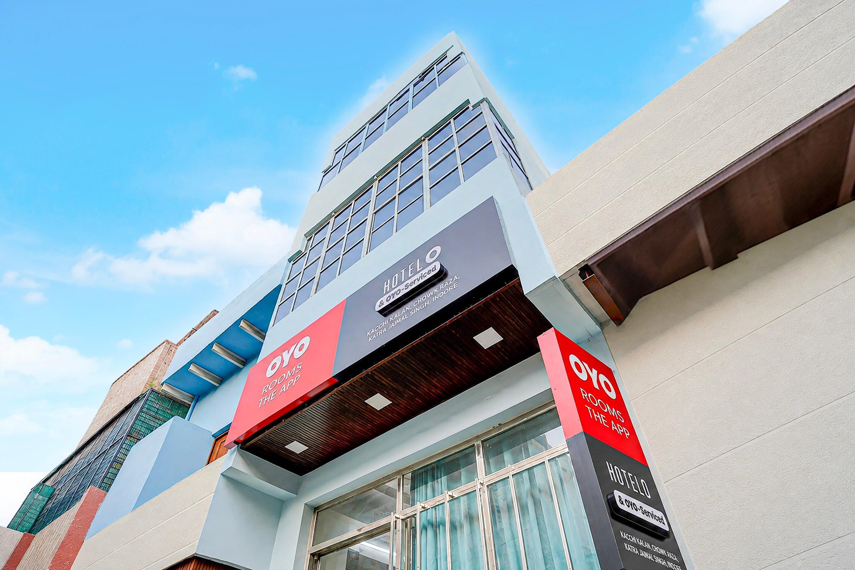 A modern hotel building with a prominent sign for 'OYO Rooms The App'.