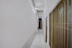A corridor with white walls, a tiled floor, and a door with a metal grille. - Classic Mathura Railway Junction (Mathura)