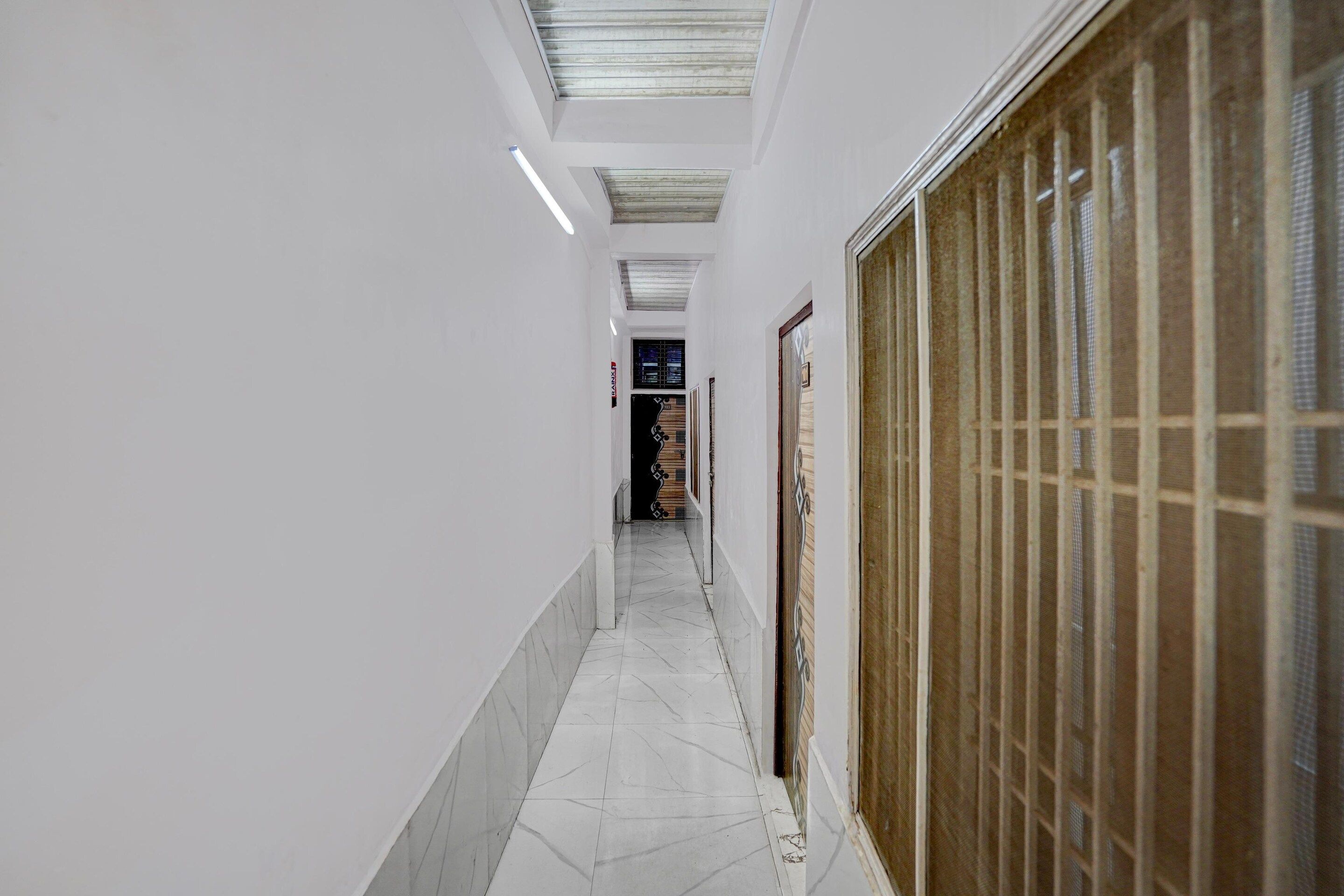 Un couloir aux murs blancs, doté d’un sol carrelé et d’une porte en bois sur le côté droit.
