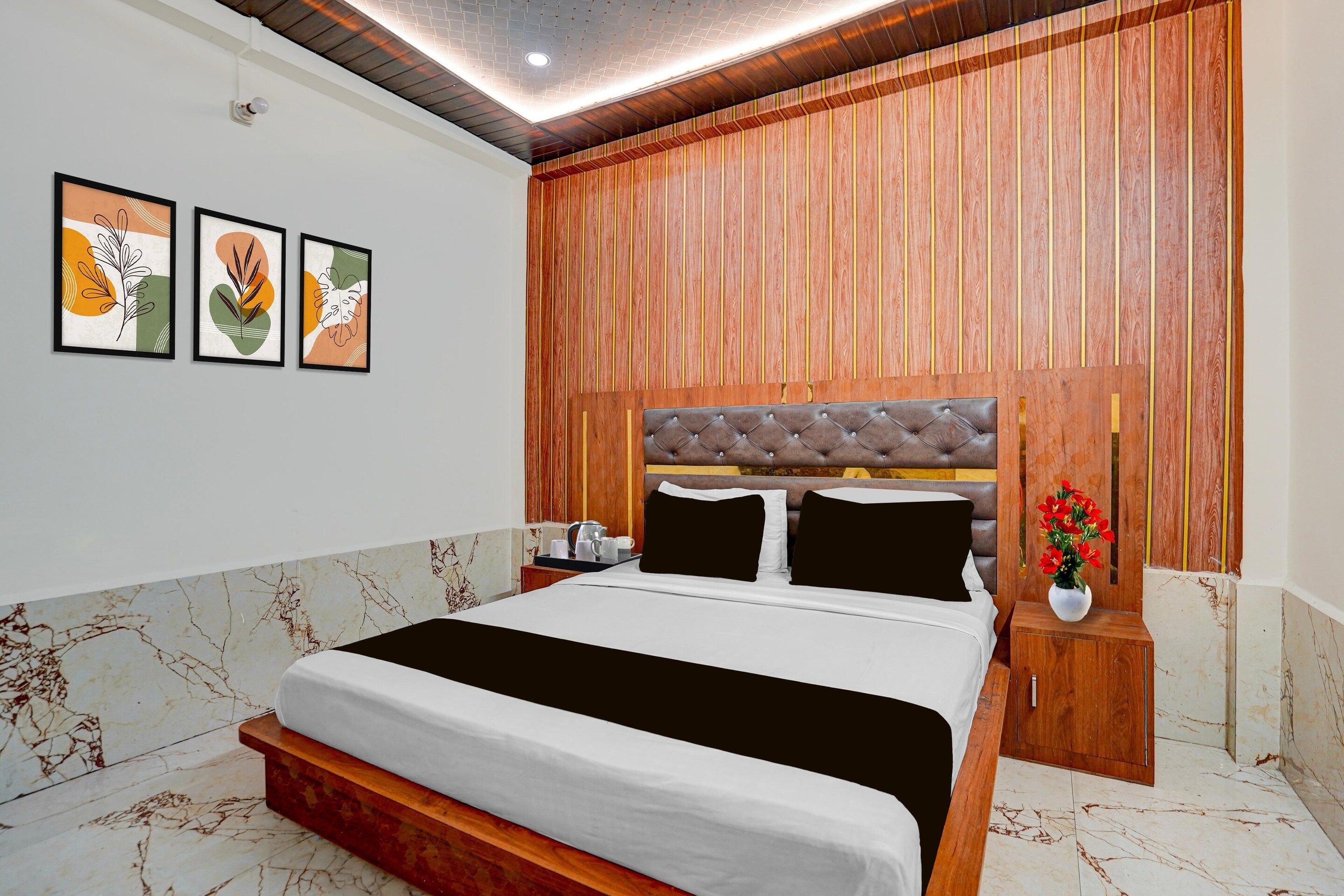 A hotel room with a bed, a nightstand, a wall-mounted camera, and framed artwork.