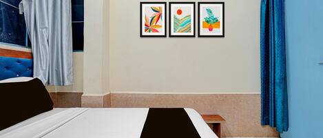 A bedroom with a bed, a nightstand, a window with curtains, and three framed artworks on the wall.