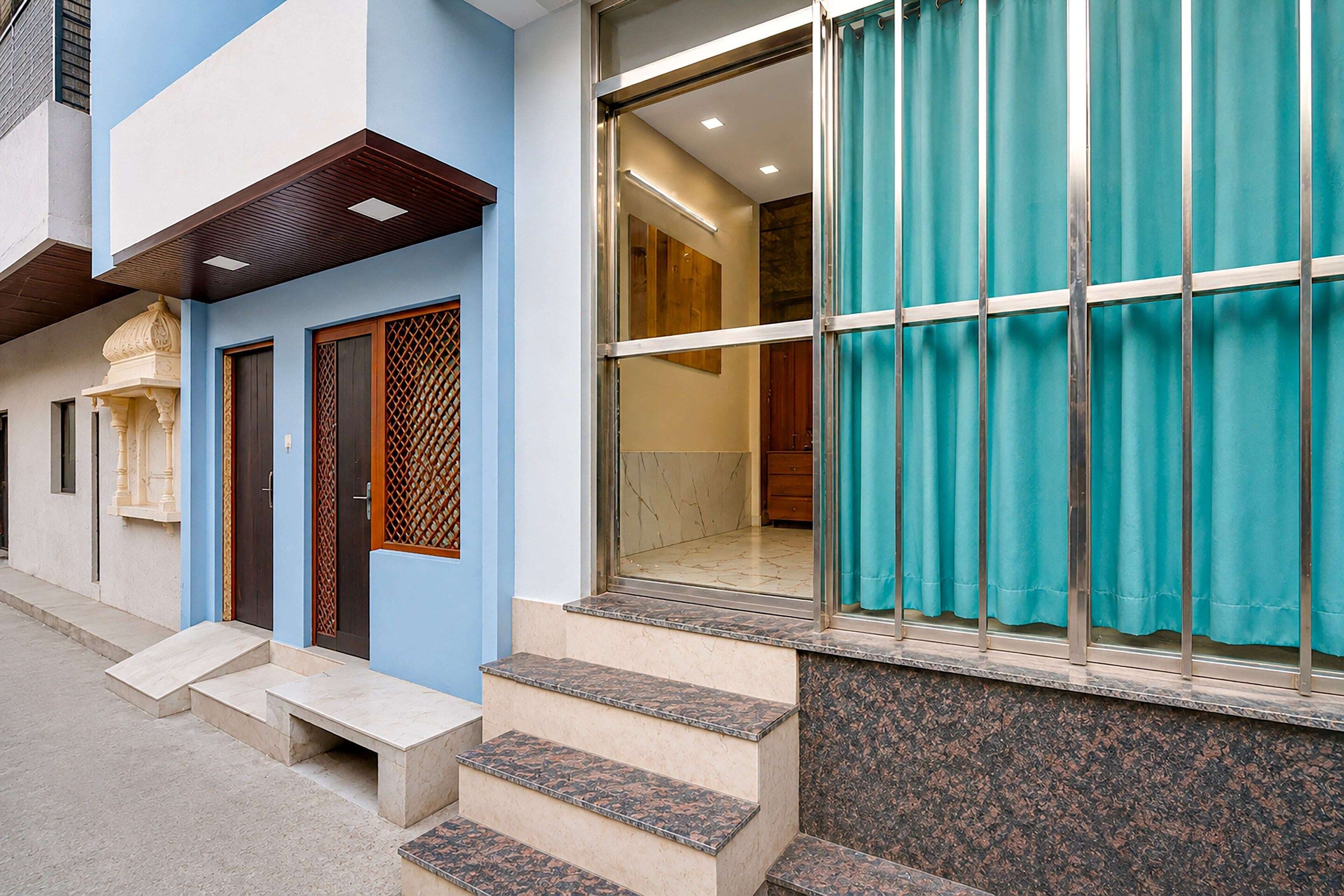 A building with a blue and white facade, a set of steps leading to a door with a decorative lattice, and a large window with a curtain.
