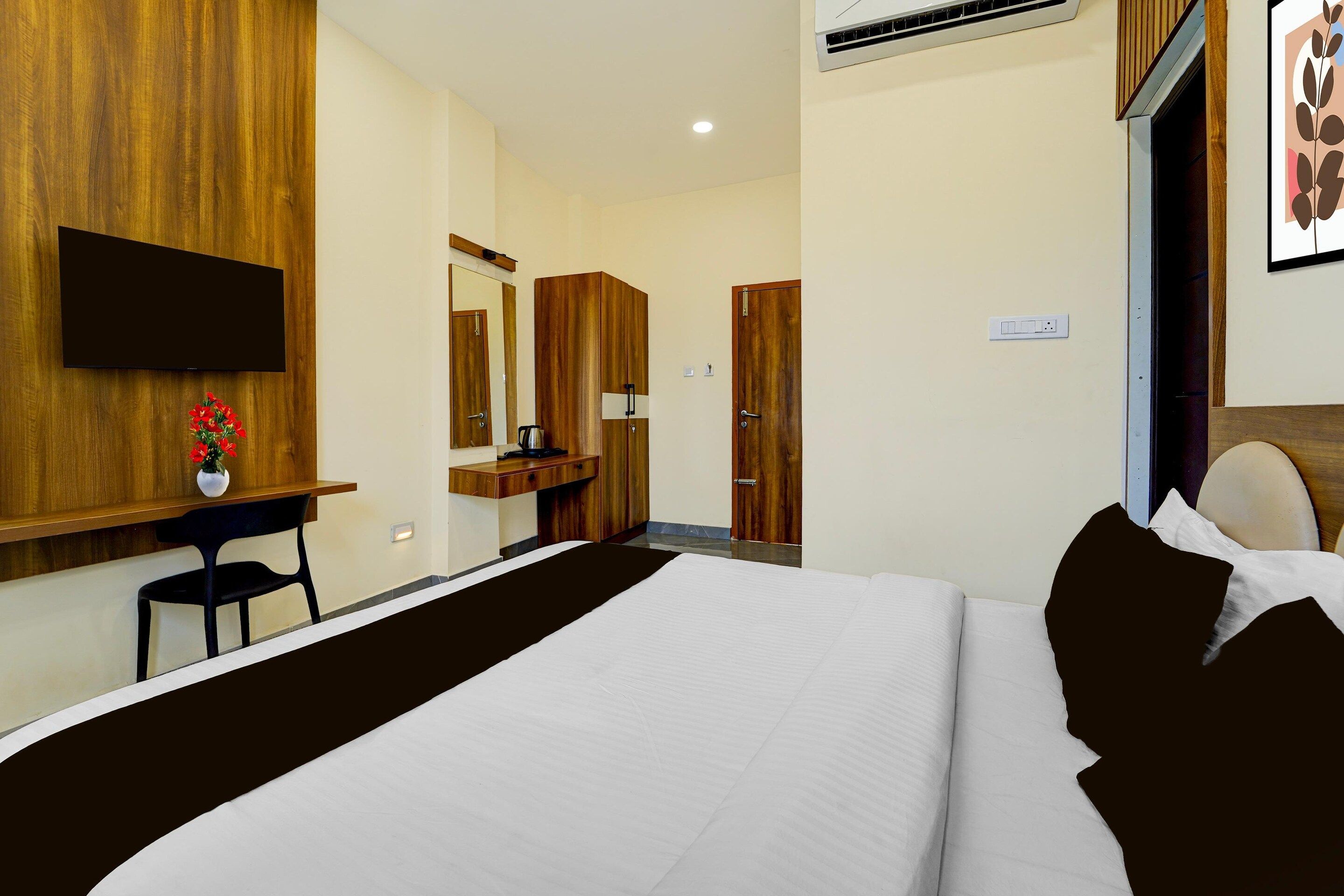 A hotel room with a bed, a desk with a chair, a television, a mirror, and a wardrobe.