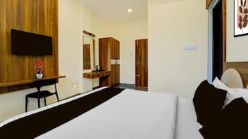 A hotel room with a bed, a desk with a chair, a television, a mirror, and a wardrobe.