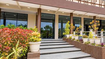 A modern building entrance with a set of steps leading to a glass door, surrounded by various potted plants.