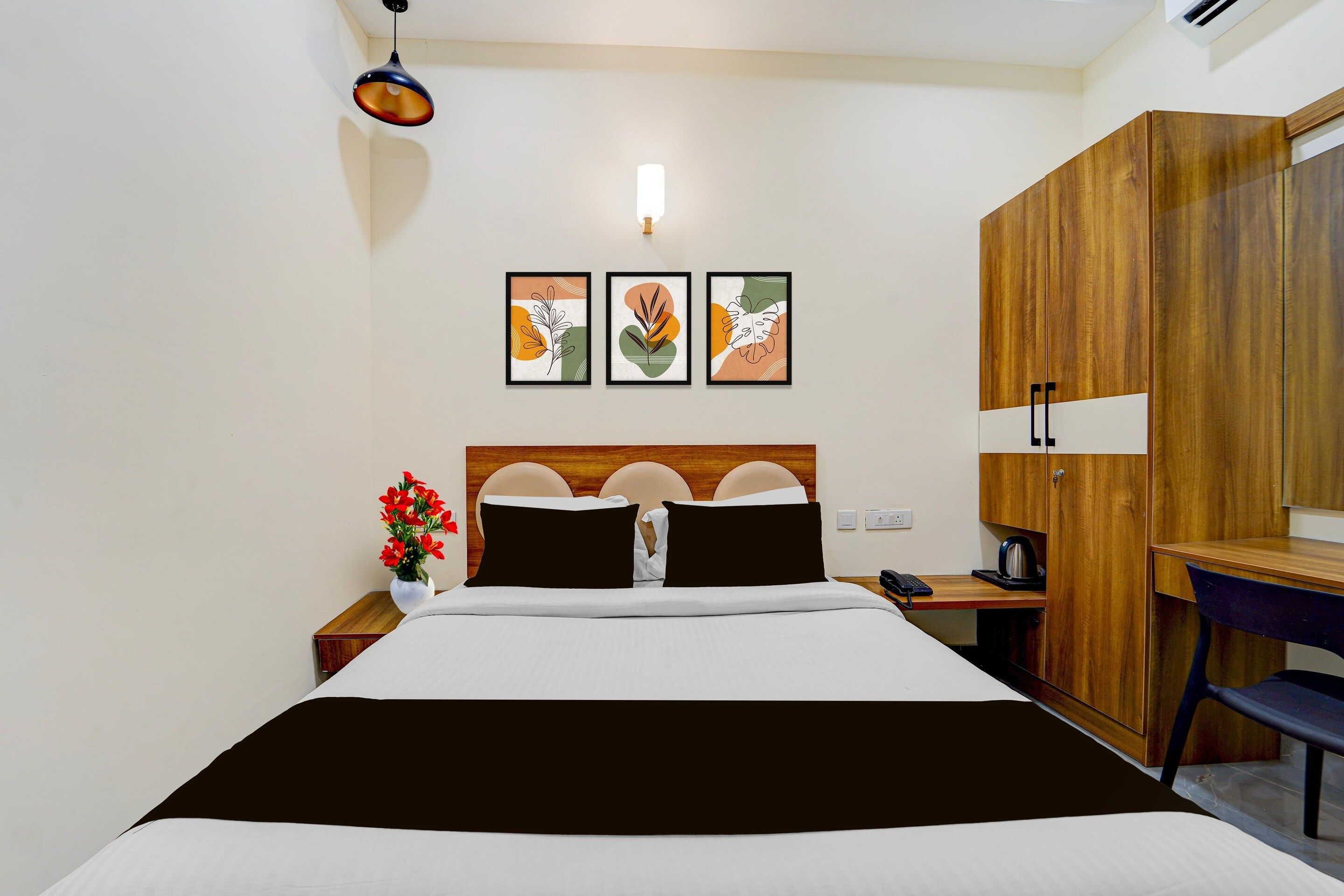 A hotel room with a bed, bedside table, lamp, artwork on the wall, and a wardrobe.