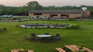 A grassy area with a small pond, picnic tables, and a building with a sloped roof.