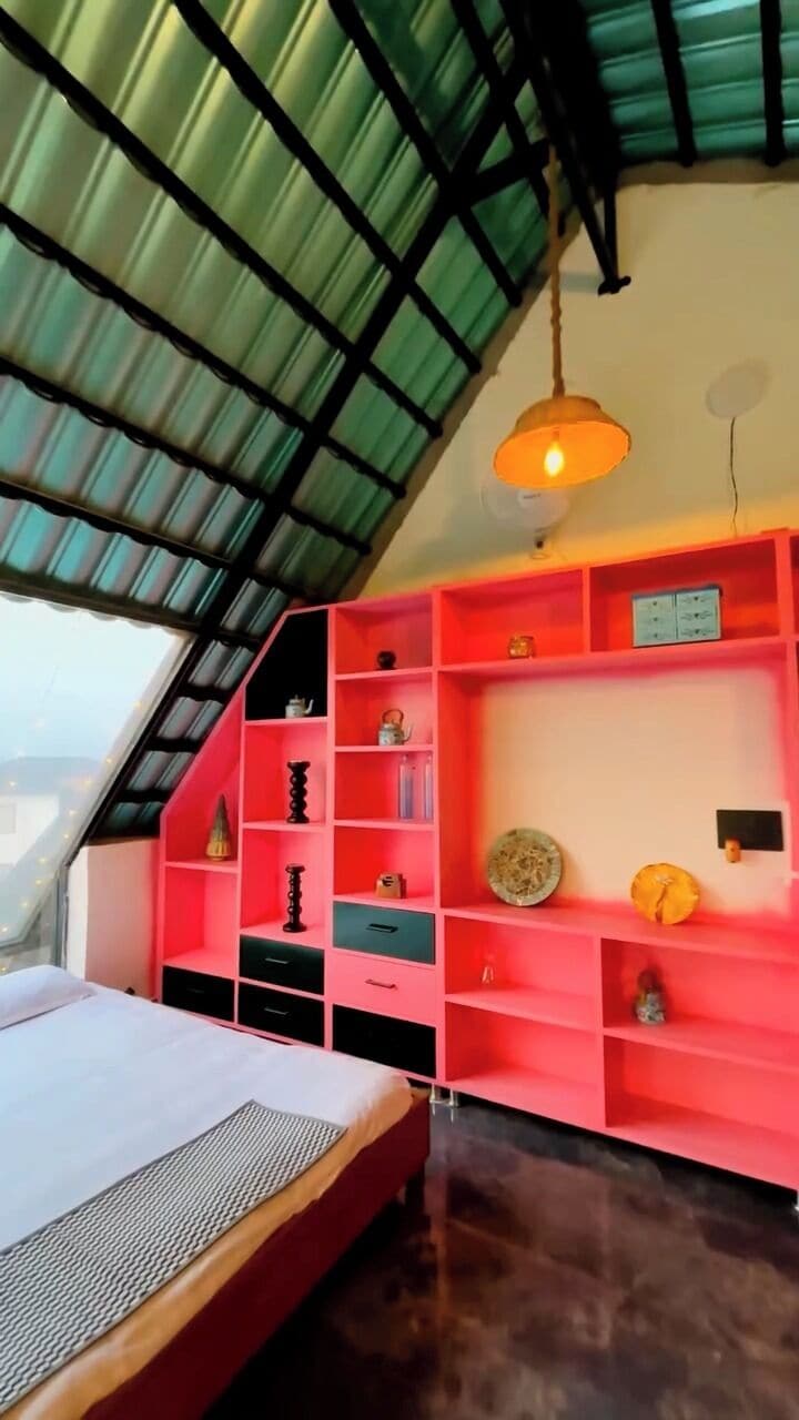 A room with a sloped ceiling, a bed, a red shelving unit, and a hanging light fixture.