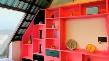 A room with a sloped ceiling, a bed, a red shelving unit, and a hanging light fixture.