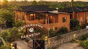 A bungalow with a gated entrance, surrounded by greenery, and labeled 'ABHYARANYAN FARMSTAY'.