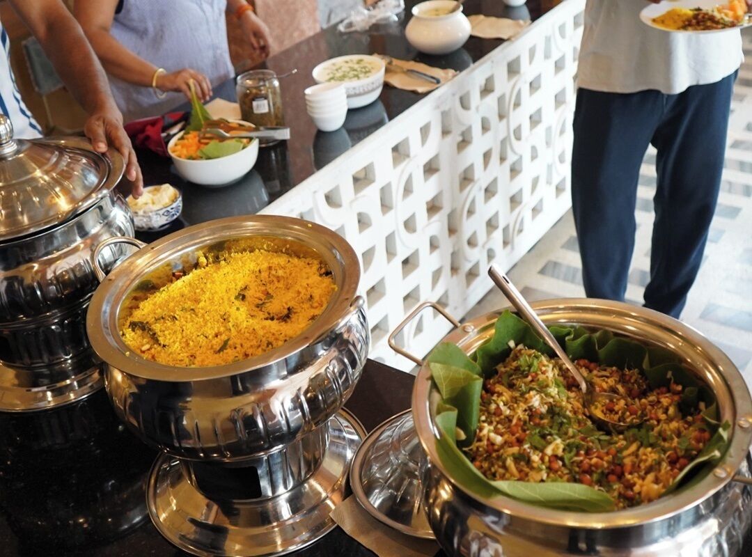 A buffet setup with various dishes in metal serving dishes, a white lattice partition, and a person serving food.