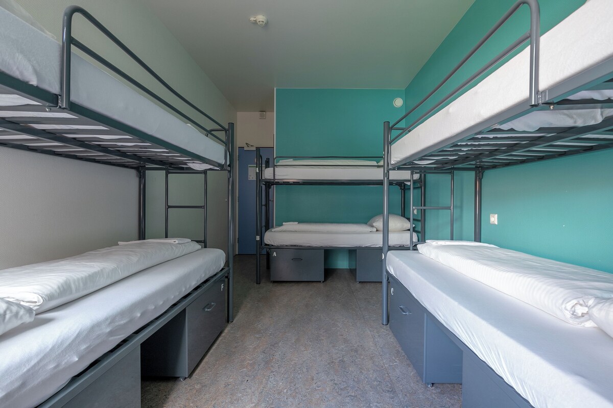 A bunk bed room with a teal wall, a ceiling light, and a door.