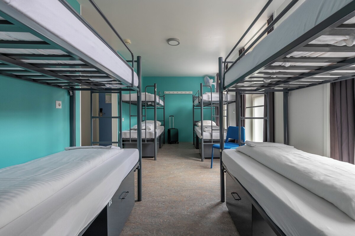 A narrow corridor with bunk beds on either side, a blue wall, and a ceiling fan.