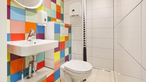 Kylpyhuoneessa on värikäs laattaseinä, valkoinen pesuallas, wc ja suihkutila.