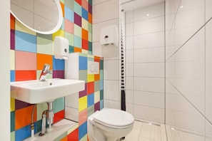 A bathroom with a colorful tiled wall, a white sink, a toilet, and a shower area. - Hans Brinker Hostel Amsterdam (Amsterdam)