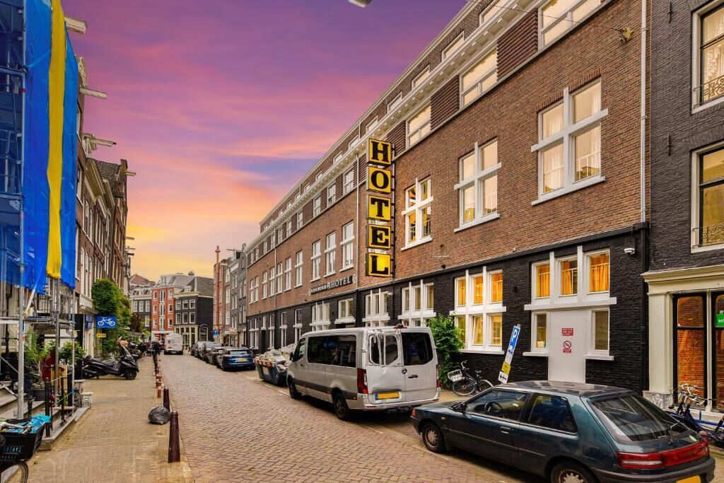 A hotel with a prominent sign on the building, a cobblestone street, parked cars, and a clear sky.