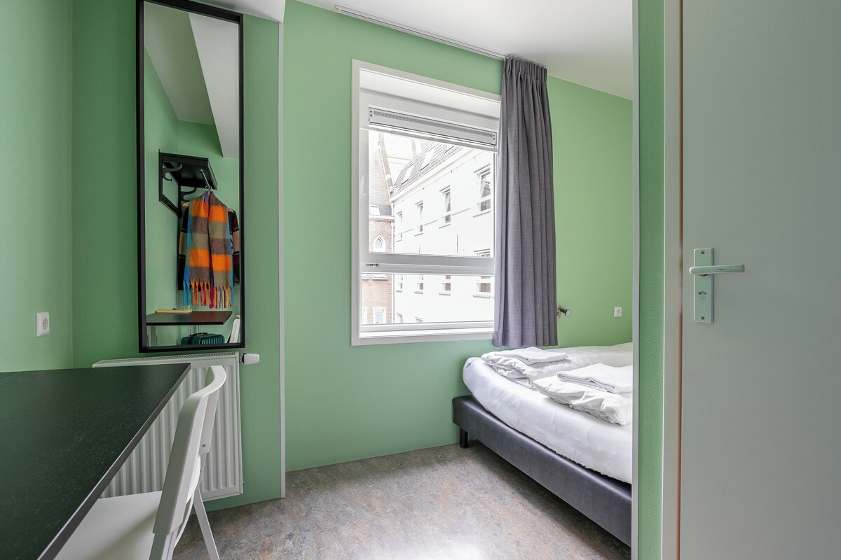 A room with a bed, a desk, a window with curtains, and a radiator.