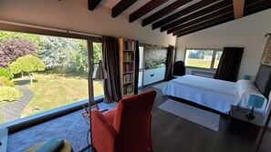 Un dormitorio con un ventanal grande, una cama, una silla roja y una estantería.