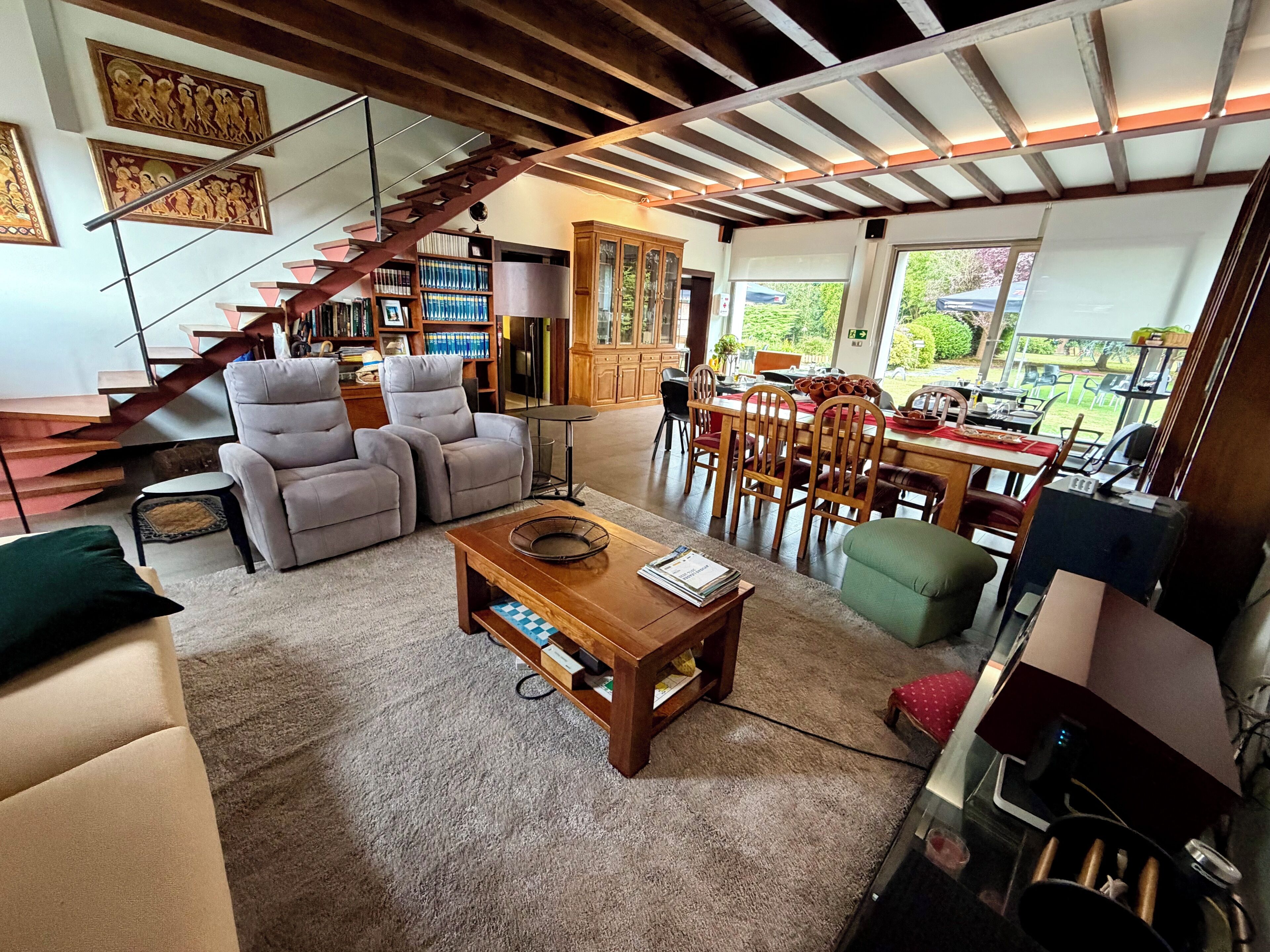 A spacious living area with a staircase, seating, a dining table, and a kitchen area.