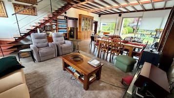 A spacious living area with a staircase, seating, a dining table, and a kitchen area.