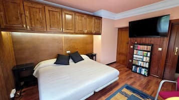 Habitación de hotel con cama, cabecero de madera, mesitas de noche, estantería y televisión.