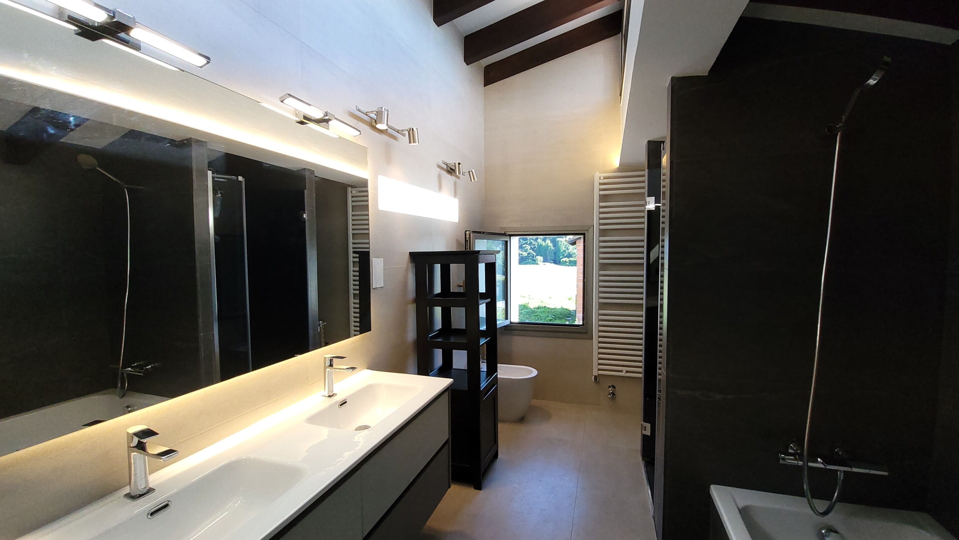 Un baño moderno con un espejo grande, lavamanos dobles, ducha y ventana que proporciona luz natural.