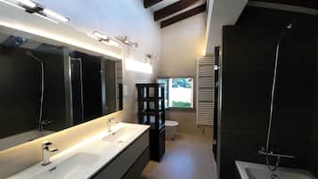 Un baño moderno con un espejo grande, lavamanos dobles, ducha y ventana que proporciona luz natural.