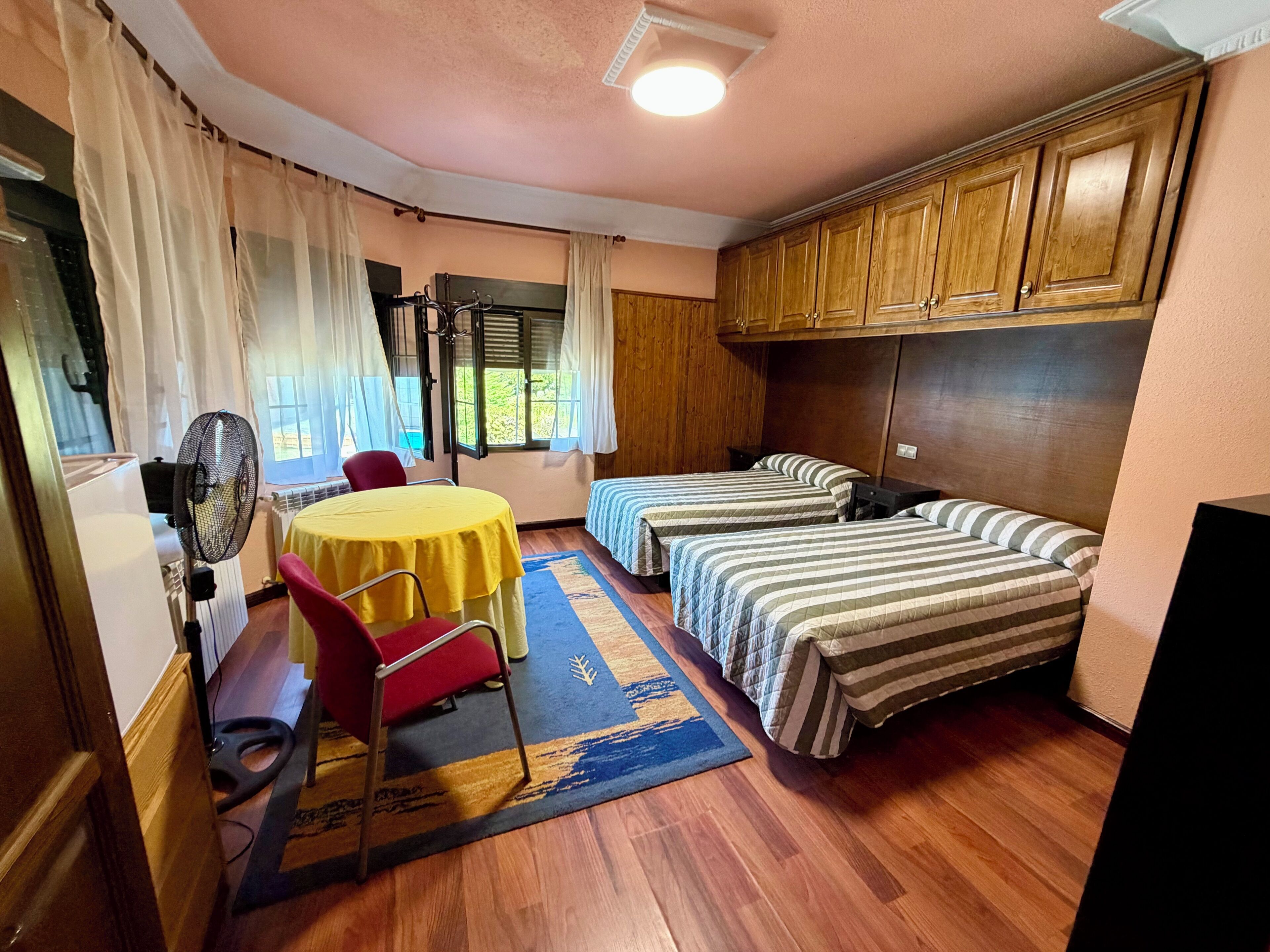 Una habitación con dos camas, una mesa, una silla y un ventilador.