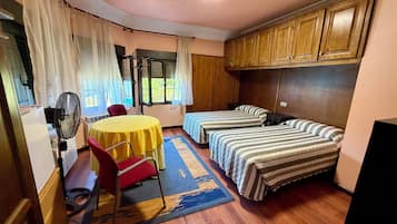 Una habitación con dos camas, una mesa, una silla y un ventilador.