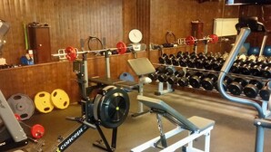 Un gimnasio con diversos equipos de ejercicio, incluyendo una prensa de banca, mancuernas y discos de pesas.