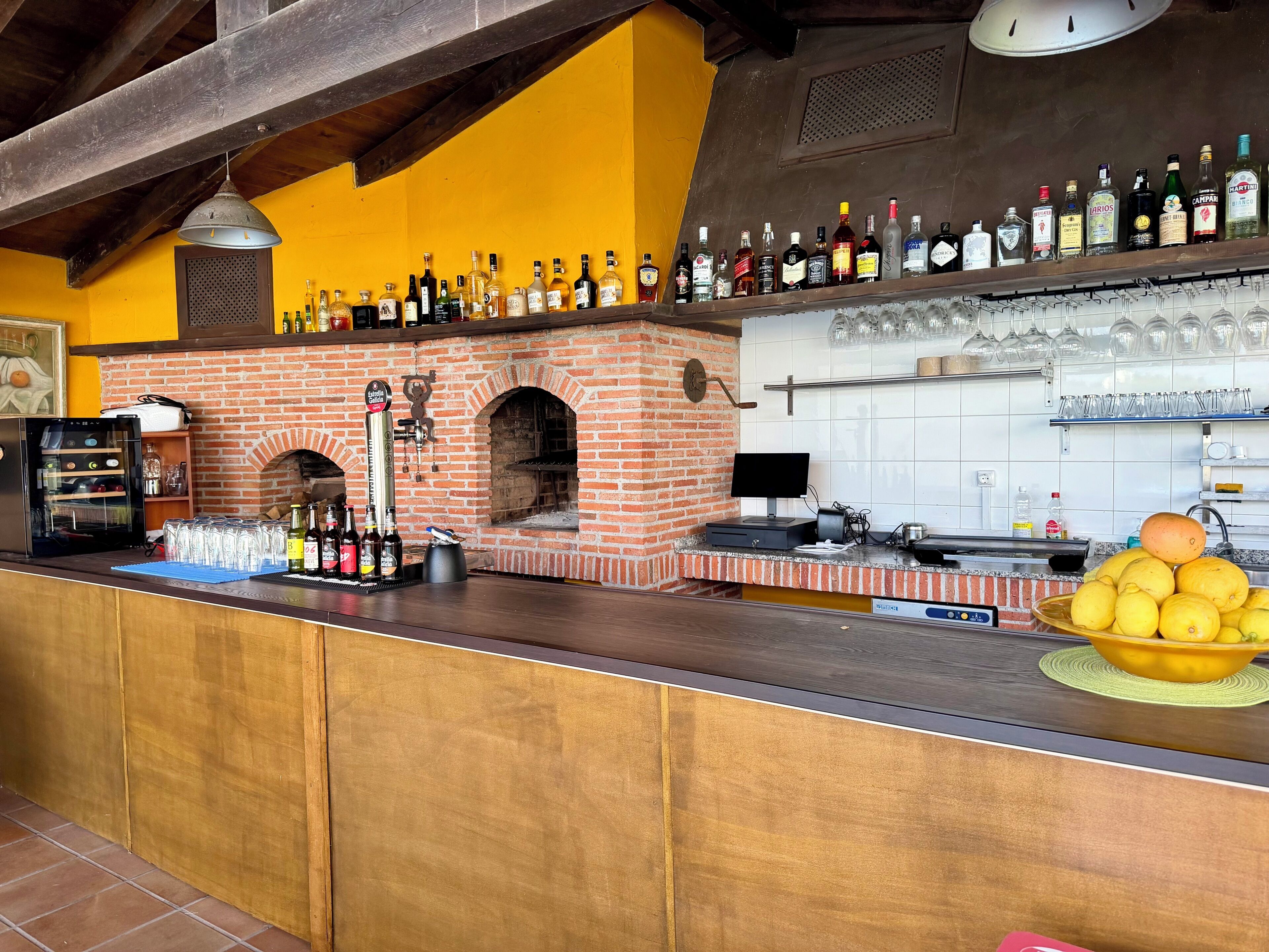 A bar area with a brick oven, a variety of liquor bottles, and a bowl of lemons.