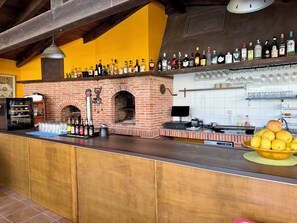 Una zona de bar con un horno de ladrillo, diversas botellas de licores y un bol de limones.