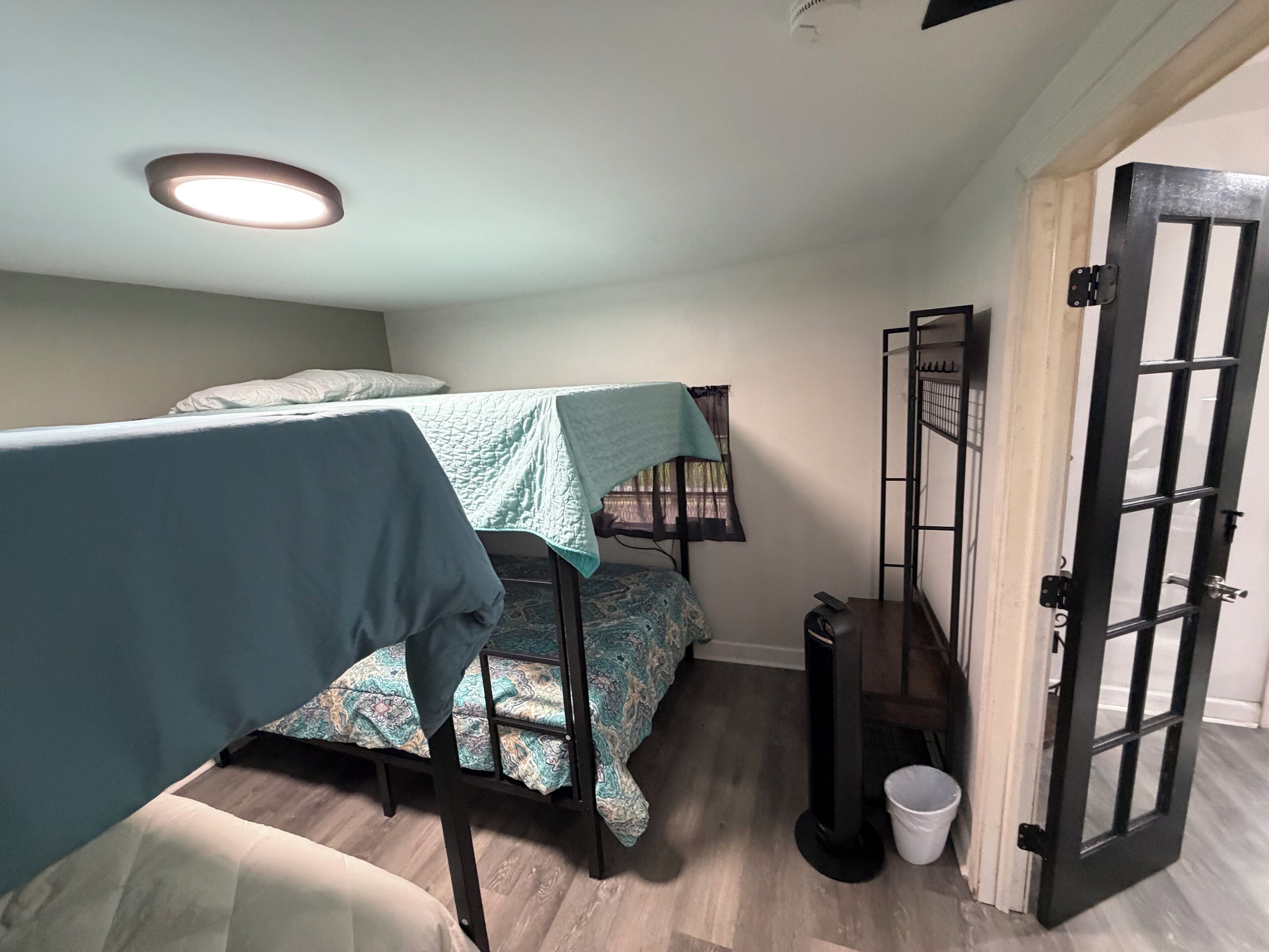 A small, compact room with bunk beds, a single bed, a desk, a chair, and a door.
