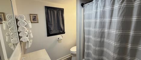 A bathroom with a toilet, sink, towel rack, and shower curtain.
