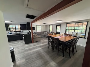 A modern kitchen with dark cabinets and a central island, a dining area with a wooden table and chairs, and a living room with a sofa and a TV. - Welcome to Shalom Shores! Your Lakefront Water Oasis in Childersburg, AL (Childersburg)