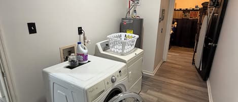 Un lavadero con lavadora y secadora de carga frontal, calentador de agua y cesta de ropa.
